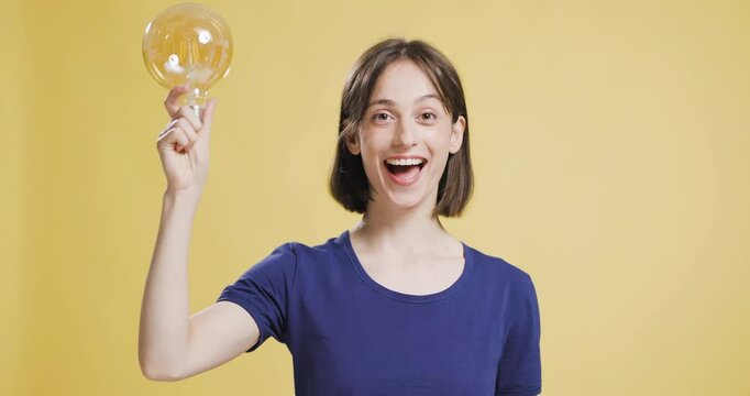 Young woman with a big light bulb expressing a bright idea on a yellow background