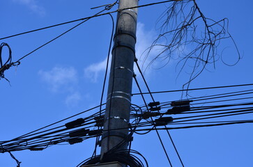 A power line pole with wires hanging from it. The sky is blue and clear. The wires are tangled and...