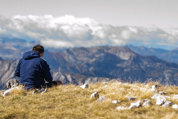 Man in a navy blue hoodie sitting on the grass at the summit of Zla Kolata in the Accursed...