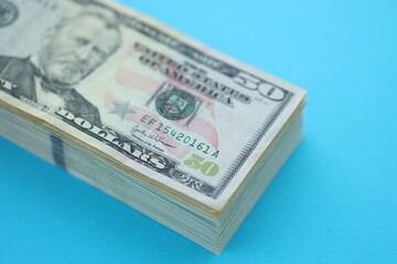 Big amount of fifty dollar bills in thick stack lies on bright blue color paper background