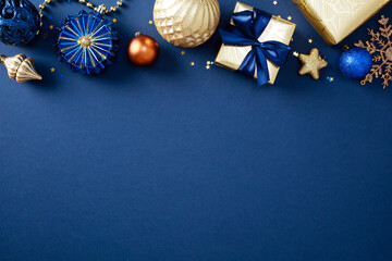 Obraz premium Frame border of stylish Christmas decorations and gold gifts on blue background. Xmas greeting card design, New Year party invitation template. Flat lay, top view, copy space