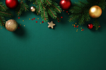 Christmas background with pine branches, colorful baubles, and glitter stars on dark green. Flat lay, top view, copy space