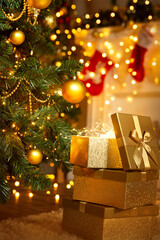 Christmas Gifts under Xmas Tree decorated with Ornaments in Room with Fireplace. Open Golden Present Box with bright Light inside over shining Christmas Lights Garland Background