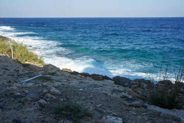Waves crashing on rocky shoreline at a tranquil coastal area during the afternoon light.