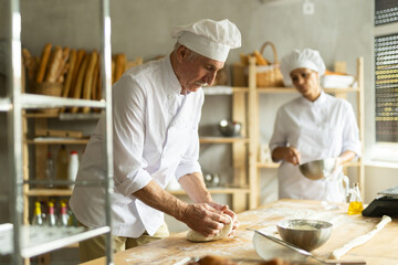 Man and woman, experienced bakers, prepare dough for baguettes and croissants together in private bakery