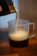Milk foam pouring into coffee in a glass cup