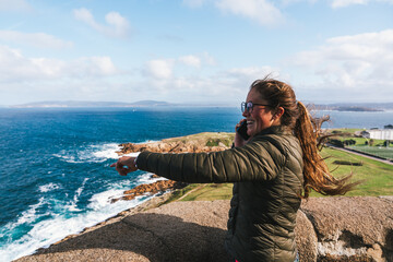 Young woman admiring ocean view and talking on phone at coastal lookout at the tower of hercules