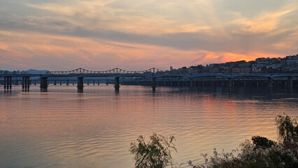 서울의 한강에서 노을지는 하늘과 불빛이 반짝이는 교량이 있는 도시 경관