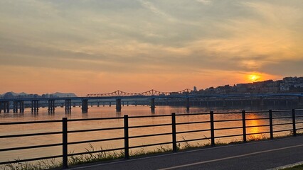 서울의 한강에서 노을지는 하늘과 불빛이 반짝이는 교량이 있는 도시 경관