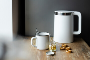 Modern electric kettle, cup of tea and cookies on wooden table in kitchen