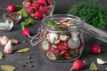Sliced radish with dill in glass jar on gray table with spices and fresh ingredients