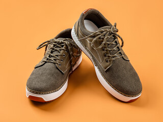 Laced up khaki canvas shoes over orange background. Pair of new brown textile shoes with white soles for active lifestyle, fitness and sports.