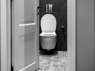 White luxury clean ceramic toilet bowl inside the toilet room with upvc door on black granite wall and marble floor, front view in modern bathroom interior, black and white style.