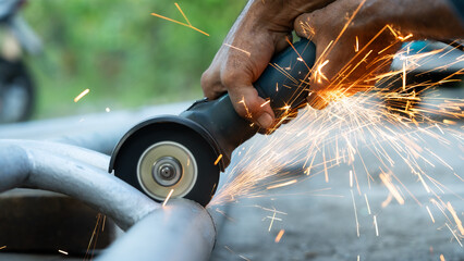 A man is using a power tool to cut through a metal pipe. The sparks from the tool are flying everywhere, creating a dangerous and intense scene. The man is focused on his task, but the sparks