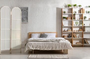 Interior of bedroom with bed, shelving unit and folding screen