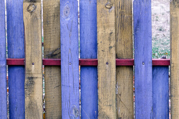 Old wooden fence made of yellow and blue planks