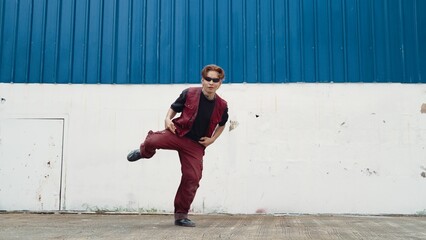 Handsome street dancer practicing break dancing at white back ground. Sport man wearing hip hop style while moving footsteps to music at street with blue background. Outdoor sport 2024. Hiphop.