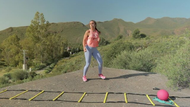 Fit Woman Performs Karate Kid Style Kick in Slow Motion in the Green Nature with Mountains. Mujer Fitness Hace Patada Estilo Karate Kid en C&aacute;mara Lenta en la Naturaleza Verde con Monta&ntilde;as

