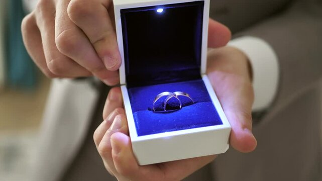 Groom's hands opening a box with wedding rings, beautifully lit