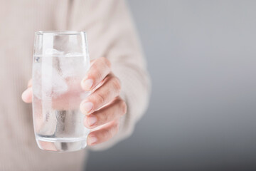 Man holding a glass of cold water with ice, showing a slight grimace due to tooth sensitivity. Image reflects the discomfort of consuming cold foods or drinks, highlighting dental health concerns