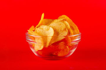 Potato chips in glass bowl isolated on red background. SIDE view