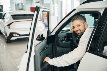 Happy man sitting in the new car with key in auto salon