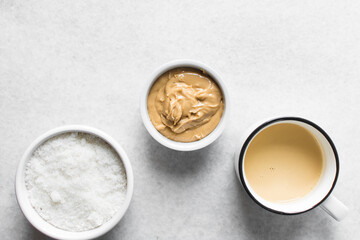 Overhead view of mise en place of ingredients for making peanut butter fudge, top view of peanut butter sugar and milk on a marble countertop, process of making peanut butter fudge