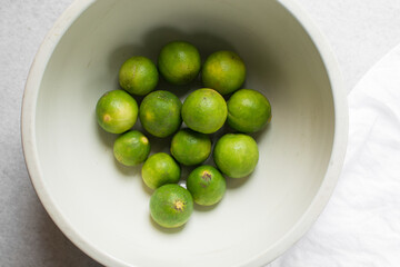 Overhead view of green limes in a white ceramic bowl, top view of organic limes in a white bowl