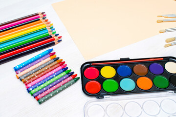 Naklejka premium Watercolor oil paints,paintbrushes,colorful pencils,pastel crayons,blank watercolor paper pad.Creativity creation.Artist's stuff.Flatlay of drawing supplies