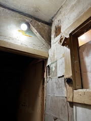 A dimly lit, aged corner of a room with cracked walls, exposed wiring, and a single light bulb...