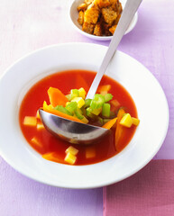 bowl of tomato soup featuring diced vegetable sits on a table, accompanied by a dish of crispy...