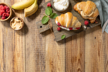 Breakfast concept, dessert french pastry. Tasty freshly baked open croissants with cream cheese and raspberry on a rustic background.