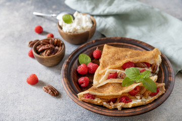 Tasty homemade sweet crepes stuffed with raspberries and cream cheese on a gray stone background. Thin pancakes, blini. Sweet dessert.