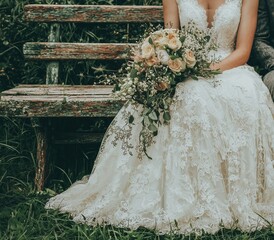 Wearing elegant attire, a bride and groom bask in each other’s company on a vintage bench nestled in a serene garden