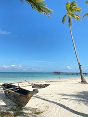 Tropical Beach Scene with Traditional Wooden Boat, Palm Trees, and Clear Blue Sky