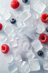 Flat lay design of scattered ice cubes and berries on an ice cold surface. Minimal frozen design with creative copy space.