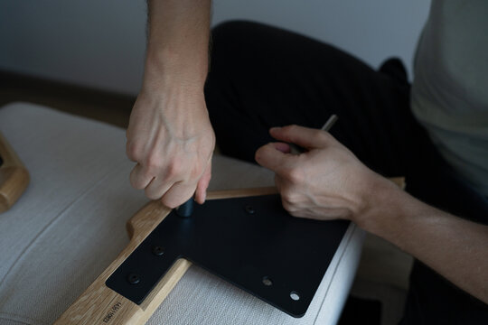 A young man is assembling a sofa by himself at home. Close up shot of a hands