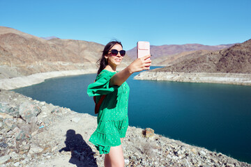 Beautiful latin tourist woman taking a selfie in the huasco valley with a damn in the background