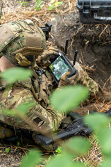 A soldier in tactical gear operates a control tablet in the field, using technology for...
