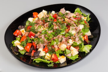 Salad of canned tuna, cheese, fresh vegetables on black dish