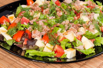 Salad of canned tuna, cheese, fresh vegetables on black dish