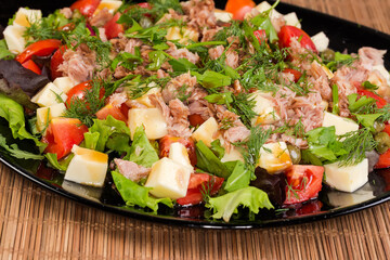 Salad of canned tuna, cheese, fresh vegetables on black dish