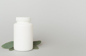 Bottles with pills and green leaves on color background