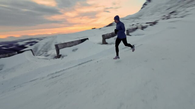 Young sportsman jogging outdoors at sunset in winter mountains. Man in sportswear leading active lifestyle