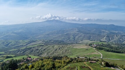 Fototapeta premium Expansive rural landscape with hills, greenery, and distant mountains under a partly cloudy sky.
