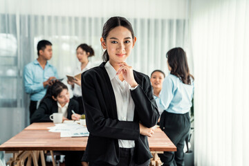 Portrait of happy young asian businesswoman looking at camera with motion blur background of business people movement in dynamic business meeting. Habiliment