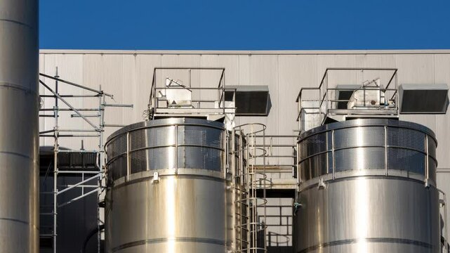 Industrial silos gleaming under a clear blue sky at a modern processing plant
