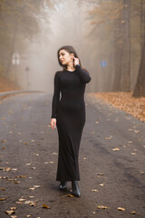 Elegant Woman in Black Dress Walking on a Misty Autumn Road