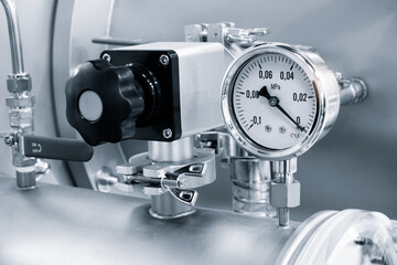 A white and black pressure gauge sits on a silver pipe. The gauge is set at zero. The black knob on...