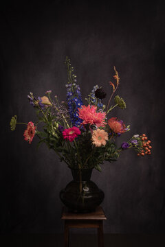 painterly still life with colorful flowers in glass vase on stool in dark renaissance style